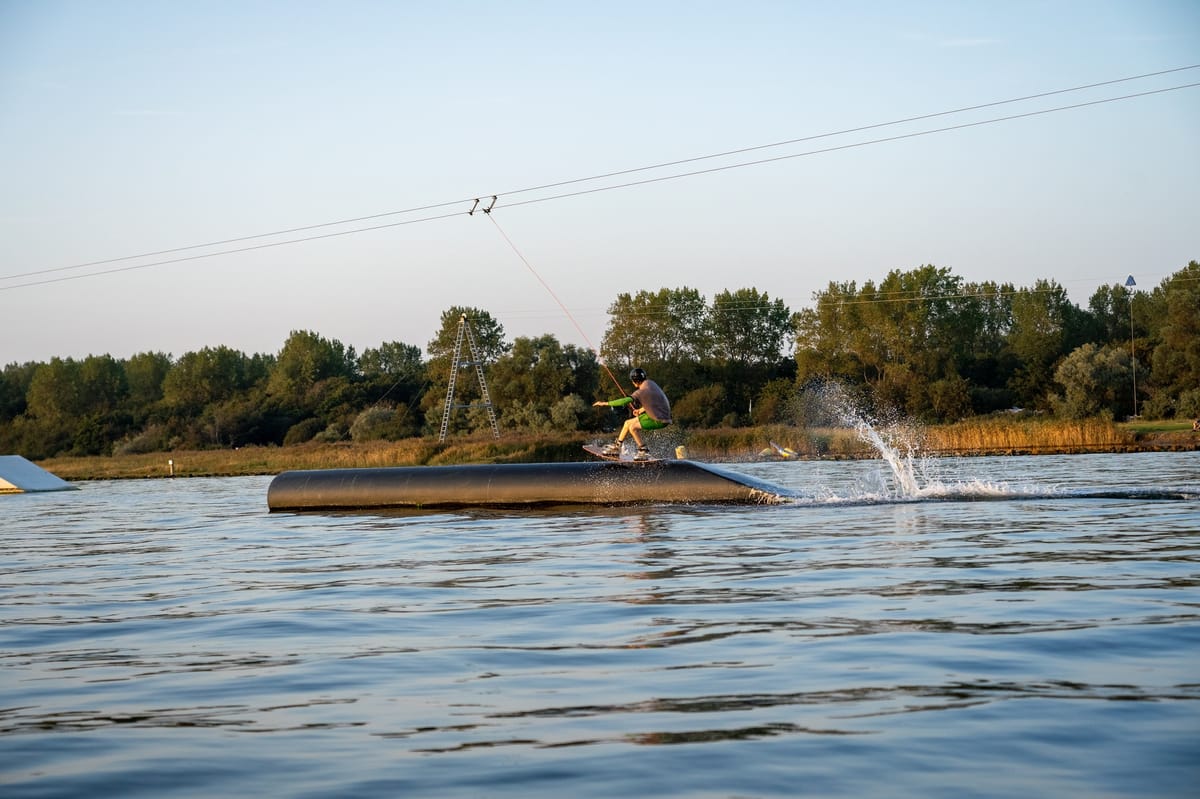 Cable wakeboarder holding a tail press across a park feature